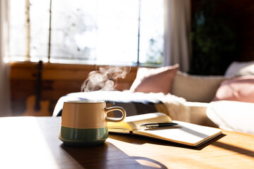 Mug of fresh coffee and book on table in log cabin on sunny day