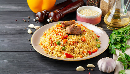 Uzbek pilaf and ingredients on black wooden background. Plov - rice prepared with vegetables and meat.