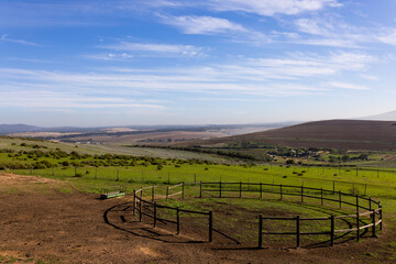 Landscape of green countryside and agricultural fields and round fence on sunny day