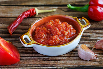 Raw uncooked Salsa or adjika sauce is traditional Mexican or Caucasus Armenian sauce with tomatoes and hot chili peppers on wodden background close up. Concept of vegetarian food