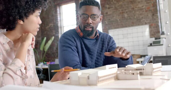 Focused diverse architect colleagues discussing work with building model in office in slow motion