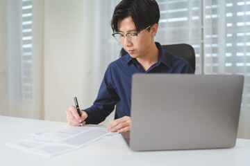 Asian businessman, male businessperson writing on paperwork with computer laptop on desk at office. Professional entrepreneur business man wear eyeglasses, sitting to working, planning on workplace. - 620362406