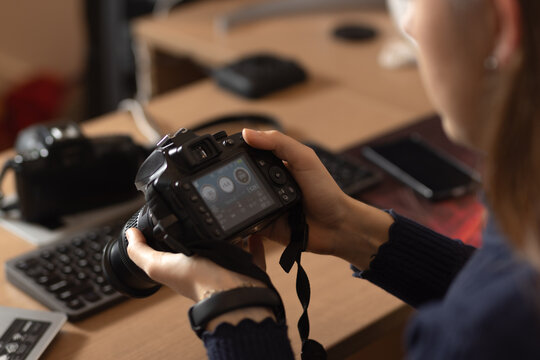 Young woman checking her parameters on professional photo camera sitting at her desk