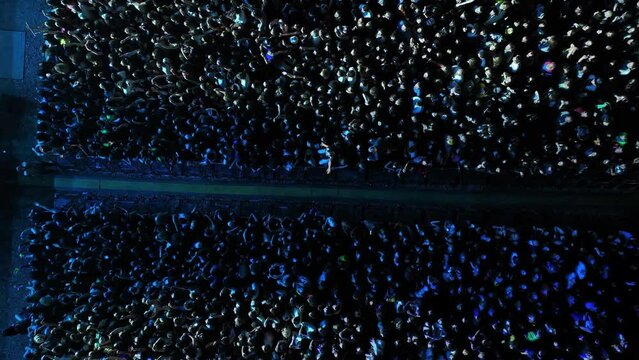 Crowd of fans are cheering at open-air music festival, back view. A large crowd of people at a music festival near the scene in the evening in the summer. Concert in the open air.Aerial view in nature