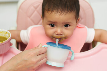 infant baby drinking a glass of water with a straw