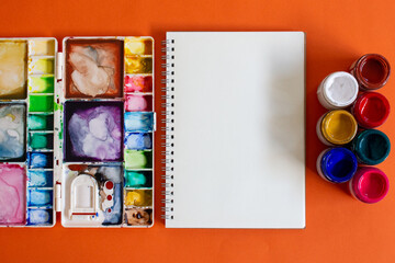 Potes de tinta guache de diversas cores, com caderno e godê de aquarela