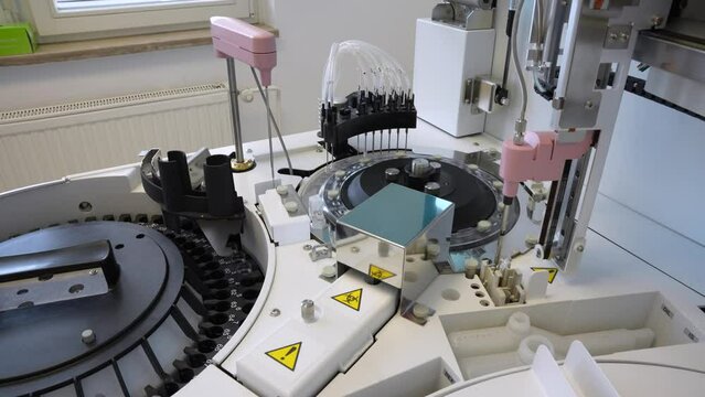 Modern looking medical machine taking reagent and applying it to blood samples in small glass cuvettes for biochemical analysis of serum and plasma in small laboratory