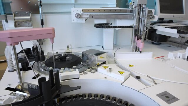 Long sharp laboratory needle on an modern analyzer moving and pipetting blood samples from rotary disk in a small medical clinic