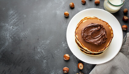Pancakes with chocolate paste and hazelnuts, on a white plate on a background of concrete, slate...