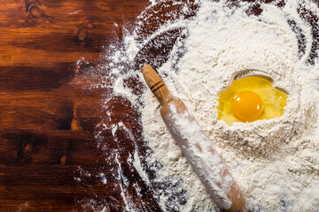 Ingredients for baking - flour, egg and rolling pin on dark wooden table with space for text