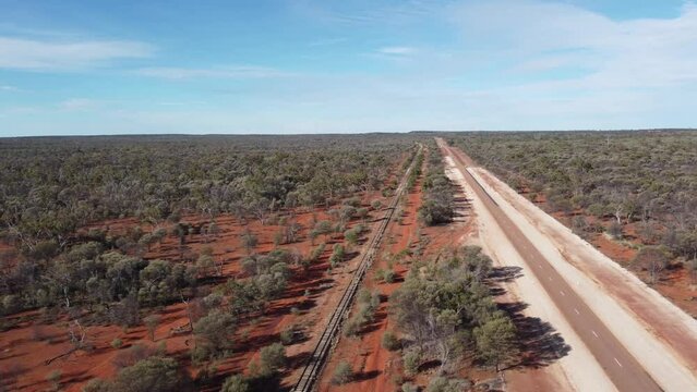 Sweeping aerial view of a parallel country road and railway line in the Australian Outback.