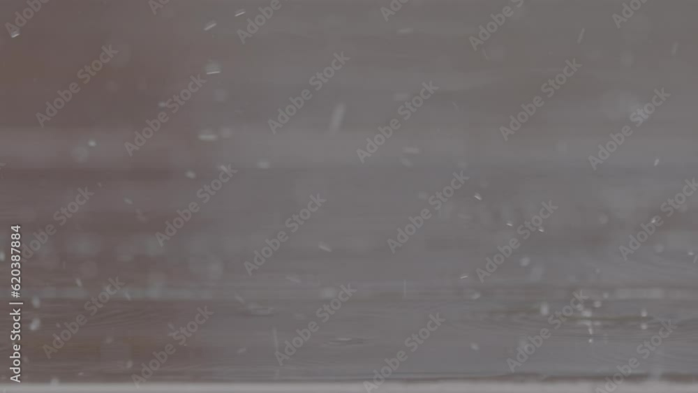 Poster close up shot of rain drops falling on a wooden table making splashes with chairs in the background 