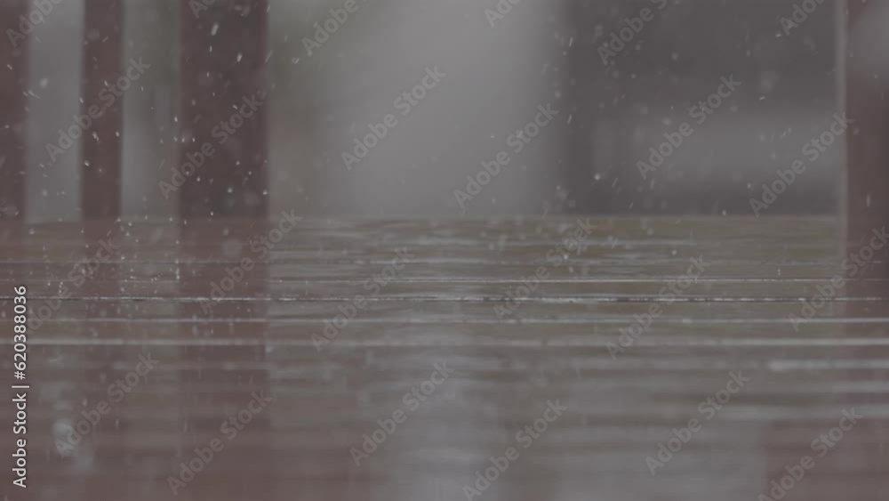 Poster close up shot of rain drops falling on a wooden table making splashes with chairs in the background 