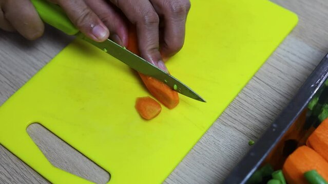 Female hand cutting or slicing carrot on yellow cutting board