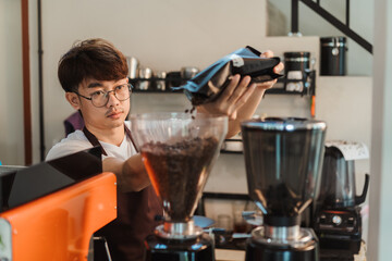 Asian man barista preparation pouring coffee bean into grind coffee in coffee shop. SME business coffee shop concept.