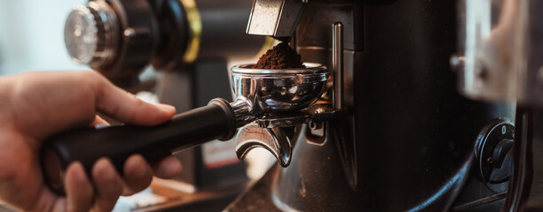 Coffee grinder grinds fresh coffee beans into a portafilter for  espresso machine. Barista grind coffee bean with grinder machine. Selective focus.