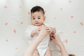 Top view mother wearing clothes to her baby. Asian family mother’s day. Baby healthcare hygiene...