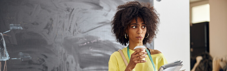 Stylish African-American designer drinks beverage at table near