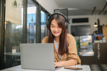 Asian woman wearing brown shirt sitting and listening to music on headphones and use a notebook computer