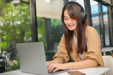 Asian woman wearing brown shirt sitting and listening to music on headphones and use a notebook computer
