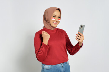 Excited young Asian women celebrate Indonesian independence day on 17 August while looking at cellphone screens isolated over white background