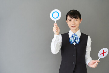 マルバツの棒を持つベストにリボンタイの制服を着た、受付業務、事務業務の女性