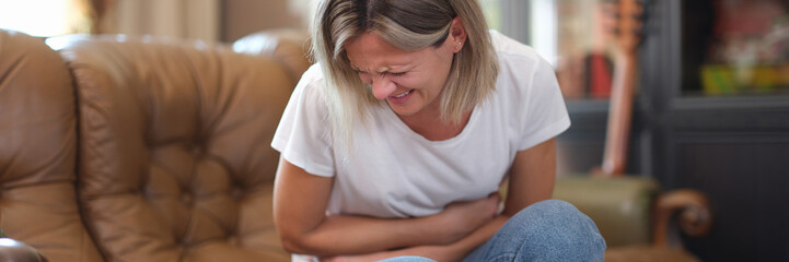 Woman sitting on sofa and touching belly writhing in pain
