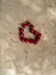 Vertical close up shot of cherries arranged in the shape of a heart on an Italian veranda in the olive tree shadow pattern.