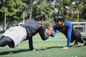Two sportsmen giving high five to each other while doing push-ups outdoors - obrazy, fototapety, plakaty
