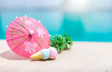 Mini Ice cream cone with paper umbrella on swimming pool edge with space on blurred blue water background, summer season concept, outdoor day light