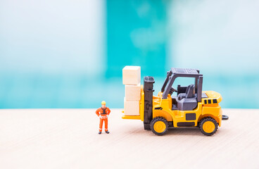 Miniature worker in safety suite with forklift truck and wooden cubes, cargo industry concept