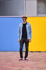 Stylish man with sunglasses and hat smiling while posing outdoors.
