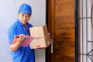 Courier holding pile of cardboard boxes, checking shipment list while standing in front door house...
