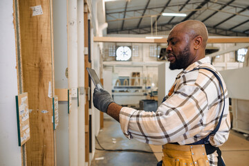 staff male black worker working in wood furniture industry factory checking selecting plywood...