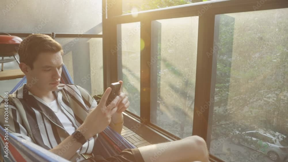 Poster man using mobile phone in a hammock - close up