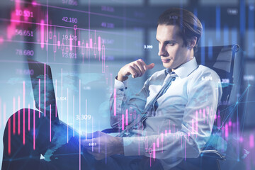 Attractive young european businessman sitting and using laptop with downward purple forex chart on blurry office background. Crisis and recession concept. Double exposure.