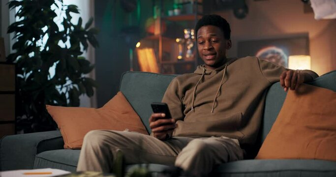 African tech enthusiast African man on a couch with a cellphone, exploring tech gadgets, and sharing his insights online.