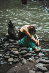 Woman Sitting on River Rocks in a Serene Nature Setting.
