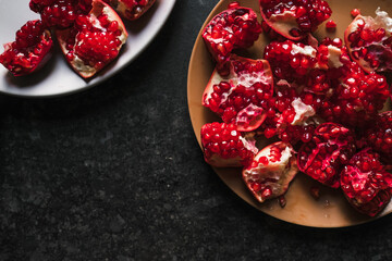 Sliced ​​pomegranate on a plate, lies on a wooden table, close-up top view.