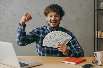 Rich young employee business Indian man wears casual blue checkered shirt hold in hand fan of cash...
