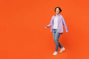 Fototapeta na wymiar Full body side view smiling happy cheerful young woman she wear purple shirt white t-shirt casual clothes walk go look camera isolated on plain orange background studio portrait. Lifestyle concept.