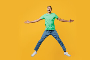 Fototapeta na wymiar Full body excited young man of African American ethnicity he wear casual clothes green t-shirt hat jump high with outstretched hands legs isolated on plain yellow background studio. Lifestyle concept