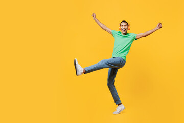 Full body happy young man of African American ethnicity he wears casual clothes green t-shirt hat listen to music in headphones isolated on plain yellow background studio portrait. Lifestyle concept.