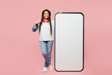 Full body young woman of African American ethnicity wear white sweatshirt casual clothes point finger on big huge blank screen mobile cell phone smartphone with area isolated on plain pink background.