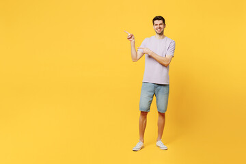 Full body young man he wear light purple t-shirt casual clothes point index finger aside indicate on workspace area copy space isolated on plain yellow background studio portrait. Lifestyle concept.