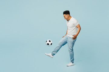 Full body side profile view happy cheerful young man fan wear t-shirt cheer up support football sport team hit soccer ball on leg watch tv live stream isolated on plain pastel blue color background.