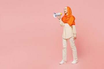 Full body young arabian asian muslim woman wear orange abaya hijab hold in hand megaphone scream announces discounts sale isolated on plain pink background. Uae middle eastern islam religious concept.
