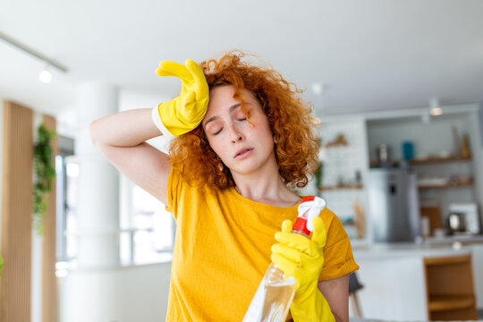Red-haired woman wearily cleans, fatigue evident on her face. With determined effort, she tidies the space, embodying the spirit of diligence and cleanliness in this evocative stock image.