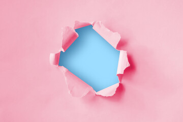 Torn hole in plain pink paper with a blue background. Concept for advertising. 