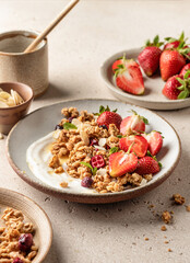 Healthy breakfast: fresh granola, muesli with yogurt, strawberry and honey on beige textured background